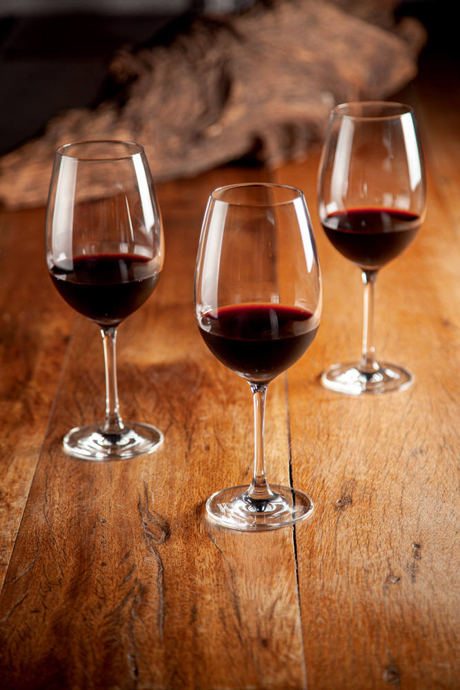 Três taças com vinho tinto sobre uma mesa de madeira.
