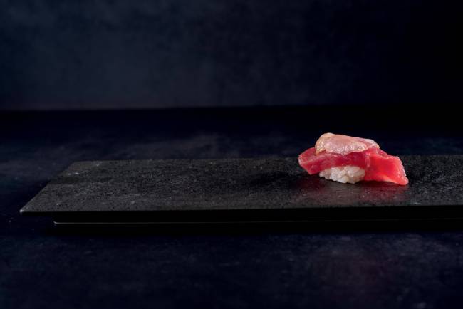 Superfície e fundo pretos com um sushi de atum em cima.
