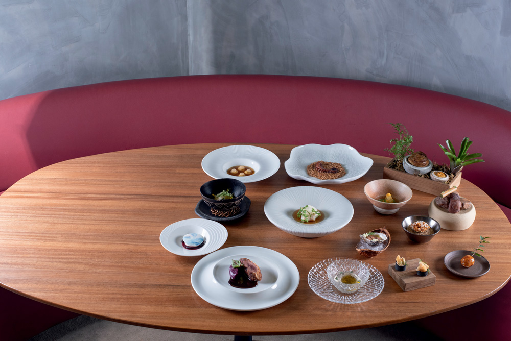 Mesa de madeira em formato oval com diversos pratos e cumbucas com comidas.