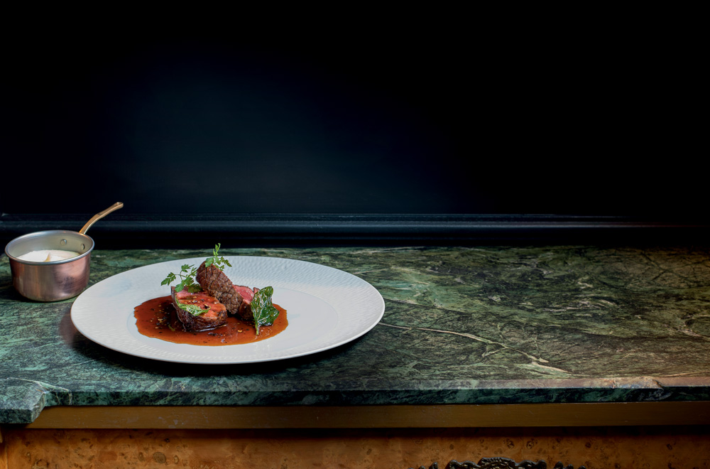 Prato branco com pedaços de carne e molho por cima sobre uma mesa de mármore.