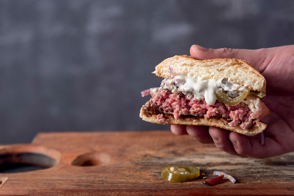 Hambúrguer cortado no meio mostra as camadas de pão, carne, molho e cebola.