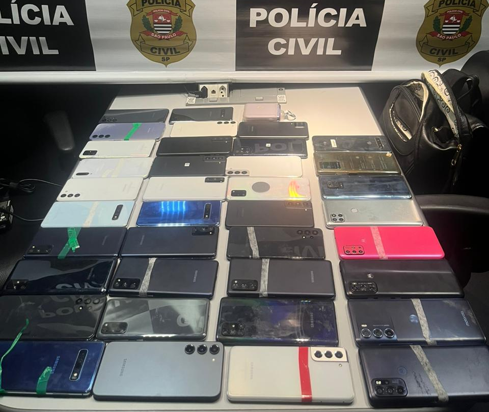 celulares em cima de uma mesa e, atrás, o brasão da polícia civil