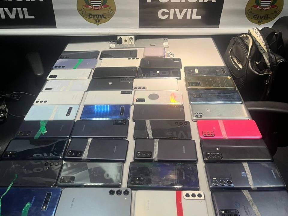 celulares em cima de uma mesa e, atrás, o brasão da polícia civil