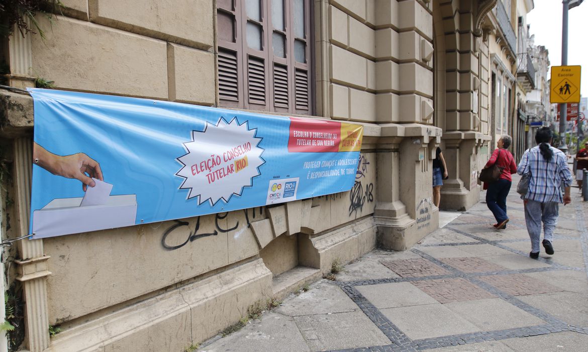 a imagem mostra uma faixa na parede de um prédio, na rua, convocando para a votação dos conselheiros tutelares