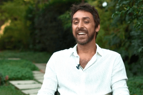 um homem branco sorrindo. ele está sentando em um jardim.