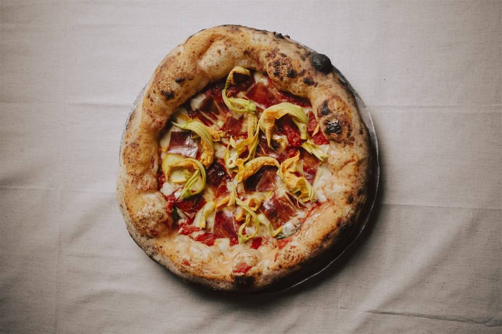 Pizza com molho de tomate e flor de abobrinha sobre tolha de mesa branca.