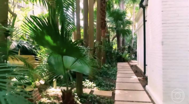 ana maria braga casa Imagem mostra lateral de casa, com caminho de pedras no meio de área arborizada