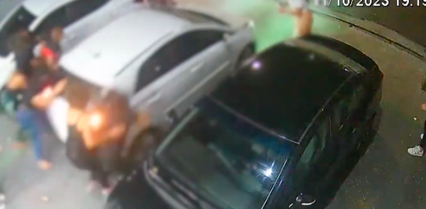 Imagem mostra vídeo de segurança. Frame exibido é o momento que mulher atropela, de marcha ré, oito pessoas que estavam atrás do carro em estacionamento de salão de beleza