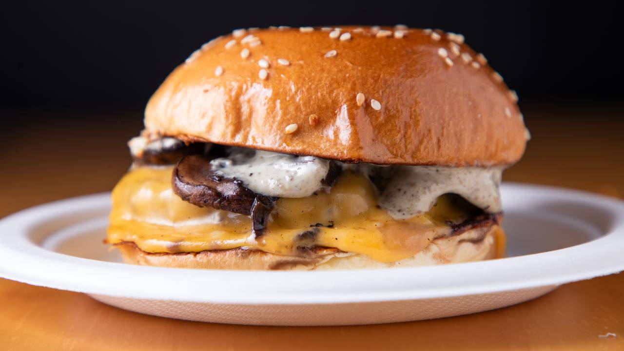 Foto mostra hambúrguer em prato. É possível ver queijo, cogumelos, maionese e pão brioche em foco