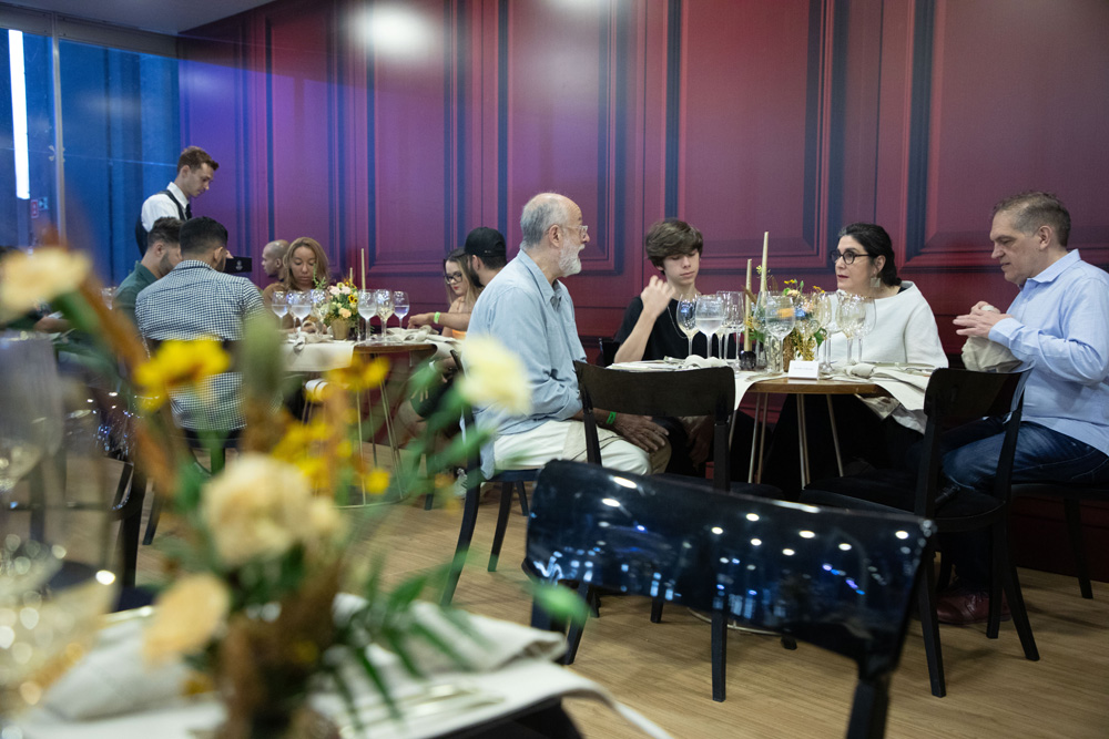 Foto tirada de longe mostra quatro pessoas sentadas em uma mesa enquanto conversam.