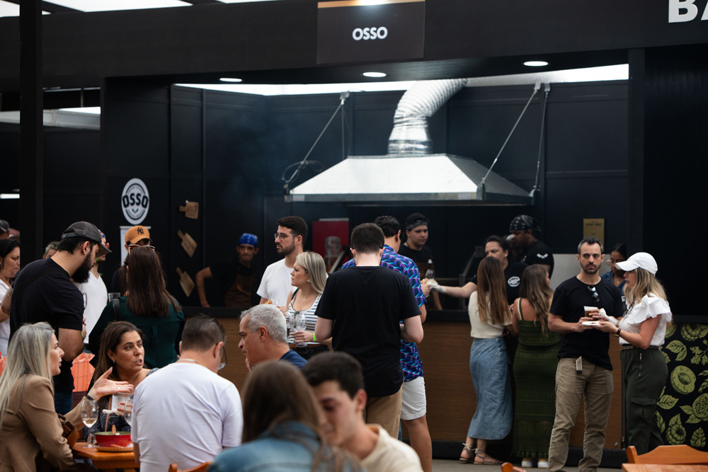 Estande do restaurante Osso, todo preto com uma coifa prateada. Várias pessoas na frente em pé e sentadas.