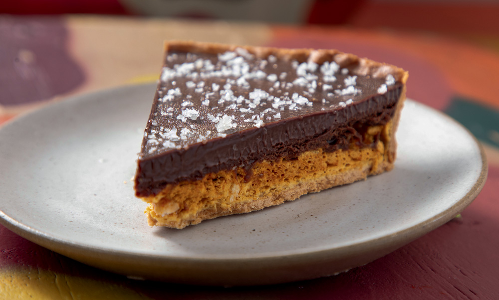 Fatia triangular de uma torta com camada de massa por baixo e de chocolate por cima.
