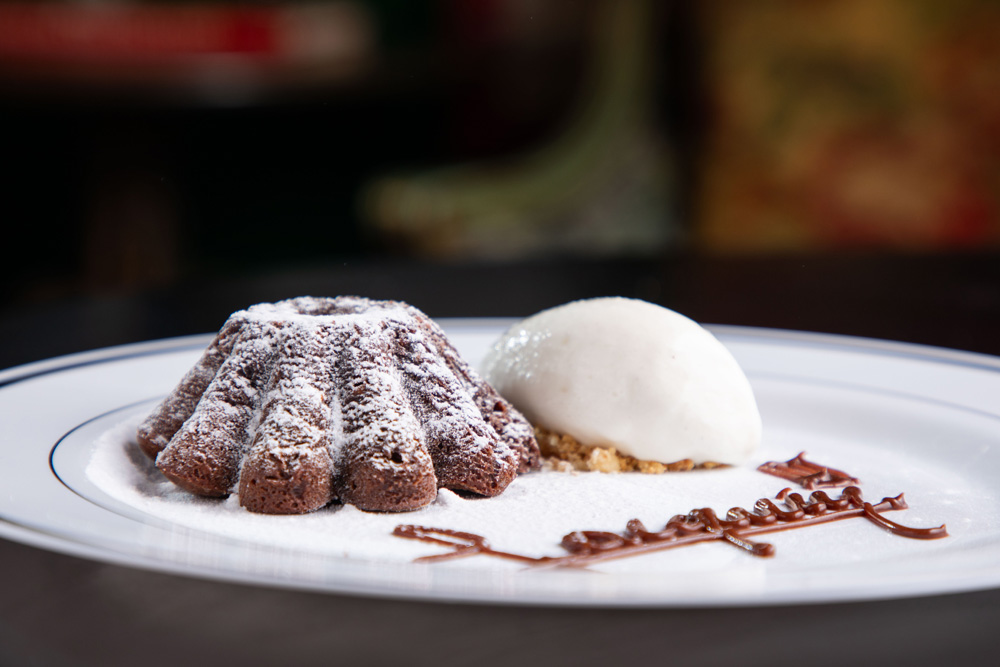 Prato branco com petit gateau e uma bola de sorvete ao lado.