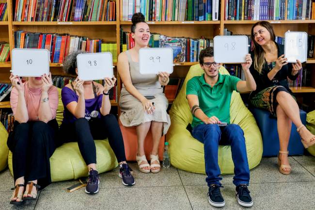 cinco pessoas sentadas em puffs em biblioteca segurando placas com notas