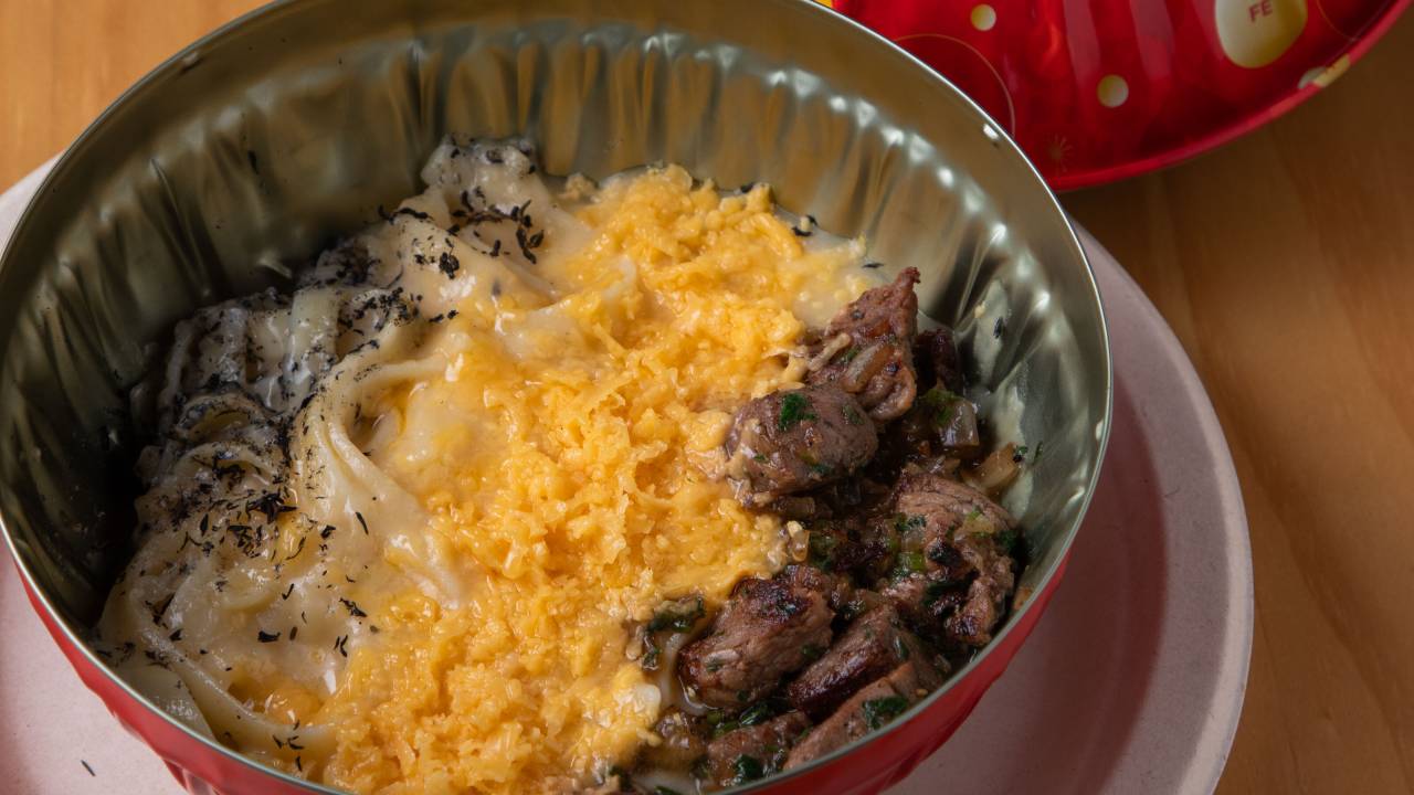 Uma lata grande e redonda com talharim com molho e queijo ralado e pedaços de carne por cima.