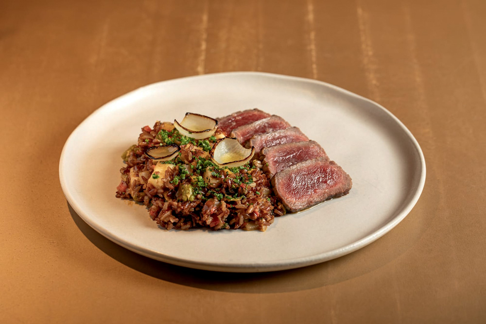 Prato de cerâmica com arroz cremoso ao lado de fatias de carn meio cruas