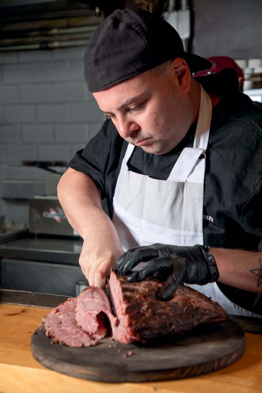 Homem com avental corta fatias de um pedaço de carne.