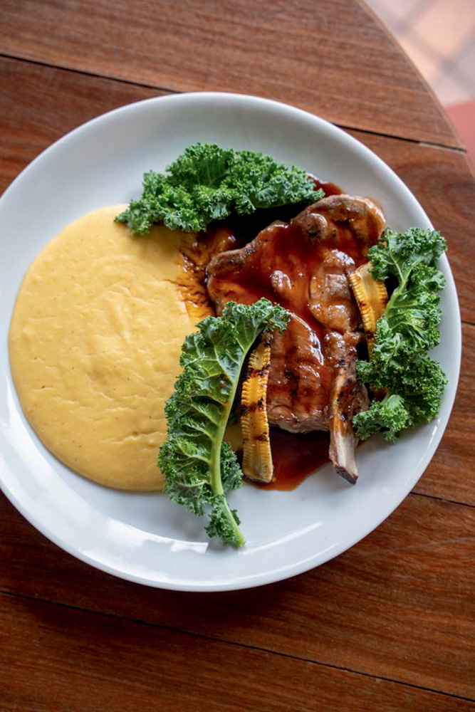 Foto aérea de prato com louça branca, polenta carne com molho e folhas de couve kale