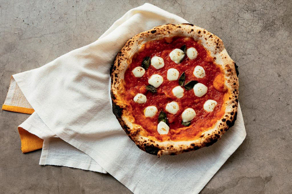 Foto aérea de pizza com molho de tomate e rodelas de muçarela de búfala sobre pano branco