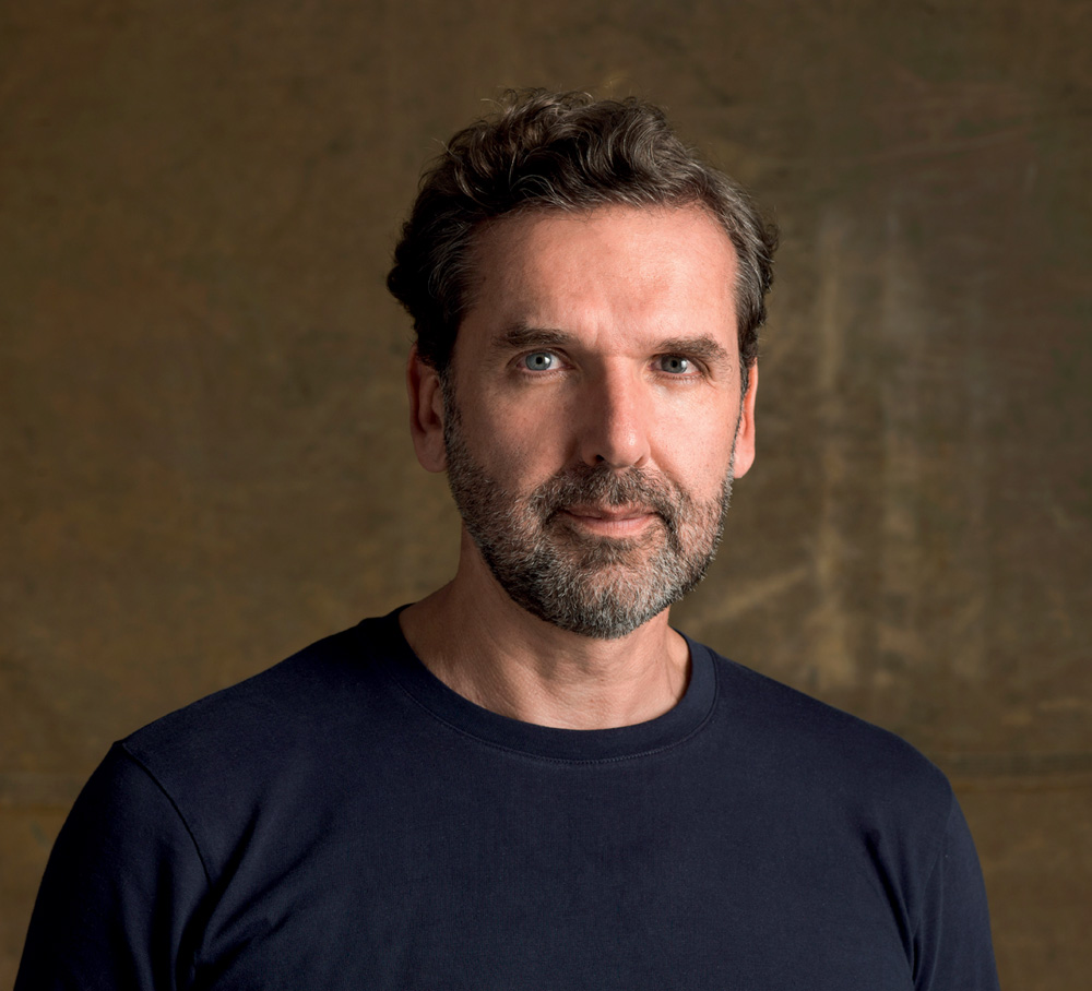 Retrato de homem branco de olhos azuis e barba grisalha e camiseta azul marinho.