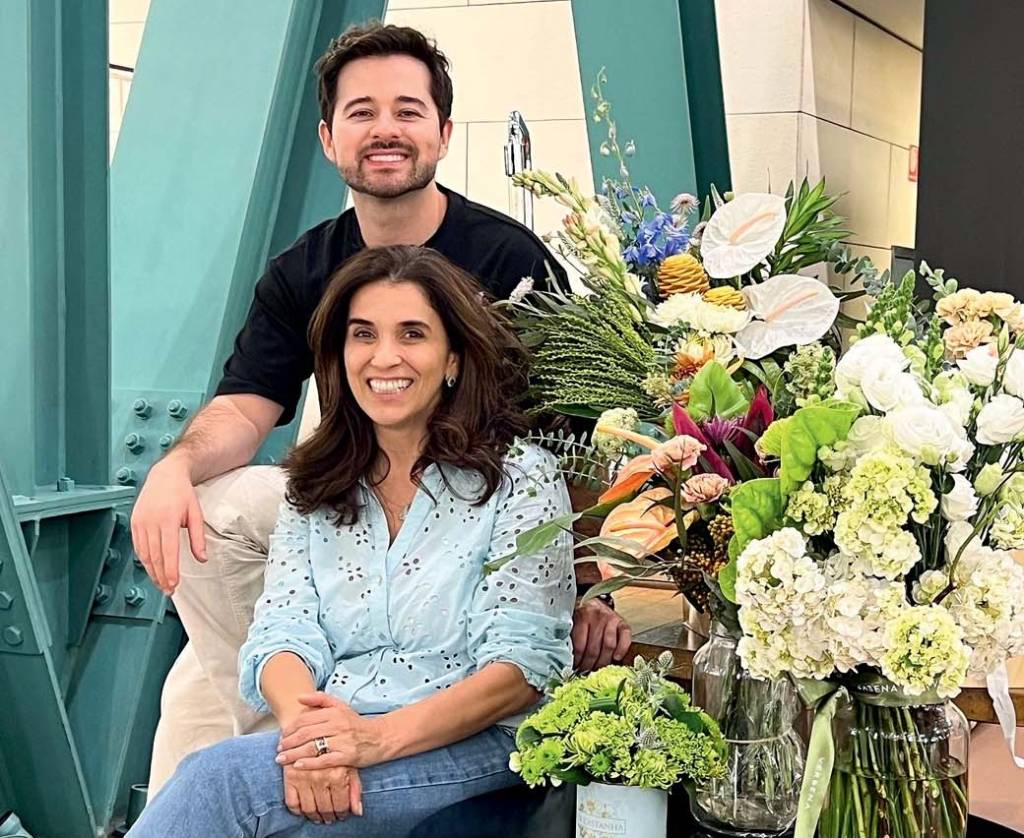 Homem negro e mulher branca posam em frente a dois quadros