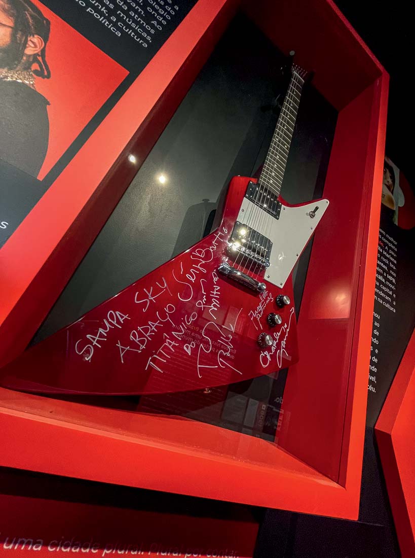 Guitarra vermelha e branca com assinaturas exibida na parede.