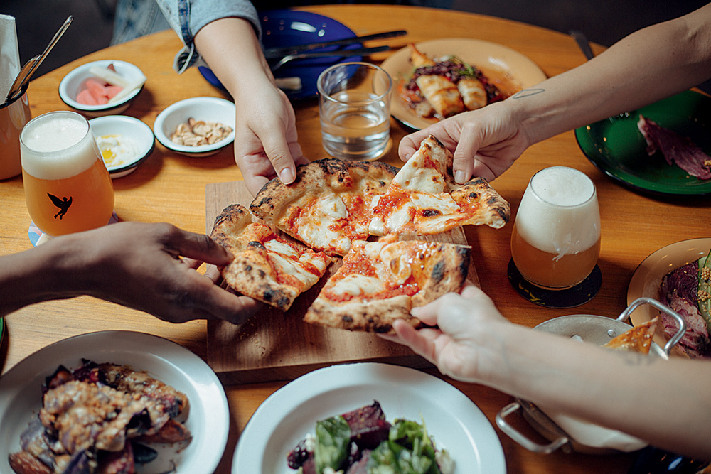 Mãos puxando pedaços de pizza com molho de tomate e queijo ao centro