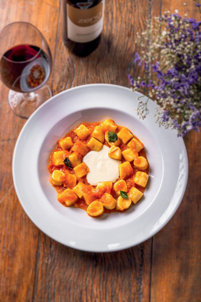 Foto de cima de um prato redondo branco com nhoque ao molho de tomate e no meio queijo derretido.