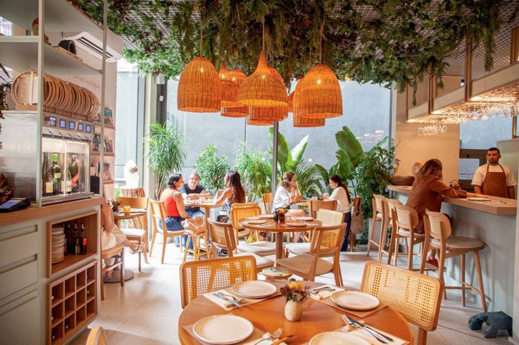 salão-do-restaurante-caracolla-com-plantas-verdes-no-teto-lustres-amarelados-e-mesas-de-madeira