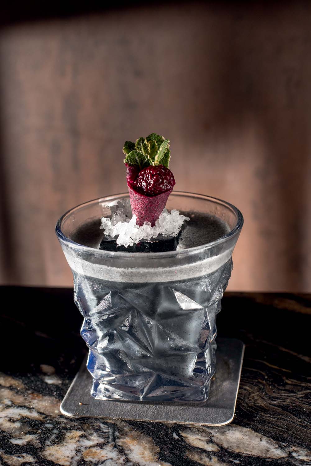 Copo de vidro com detalhes triangulares por fora com um líquido preto e um cone com fruta dentro para enfeitar.