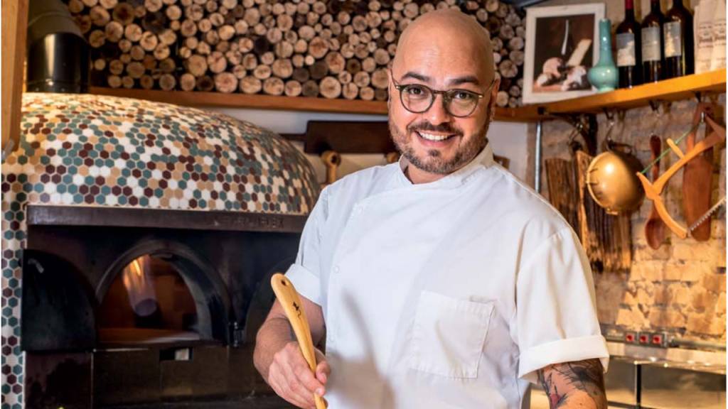 O casal Lucas Dante e Gabrielli Fleming, ele de pé e ela sentada, no salão do restaurante Cepa, no Tatuapé