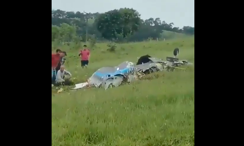 Imagem mostra destroços de avião em área com capim baixo. Cerca de cinco pessoas estão ao redor dos destroços