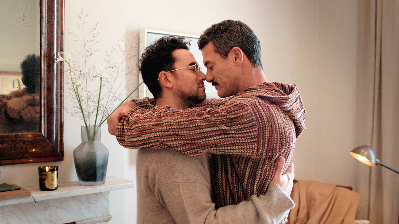 Casal de homens gays aparece abraçado dentro de sala de estar
