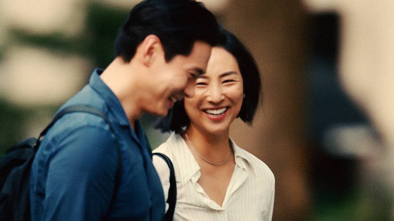 Mulher coreana sorri ao lado de homem de cabelos pretos sorrindo e aparecendo de lado