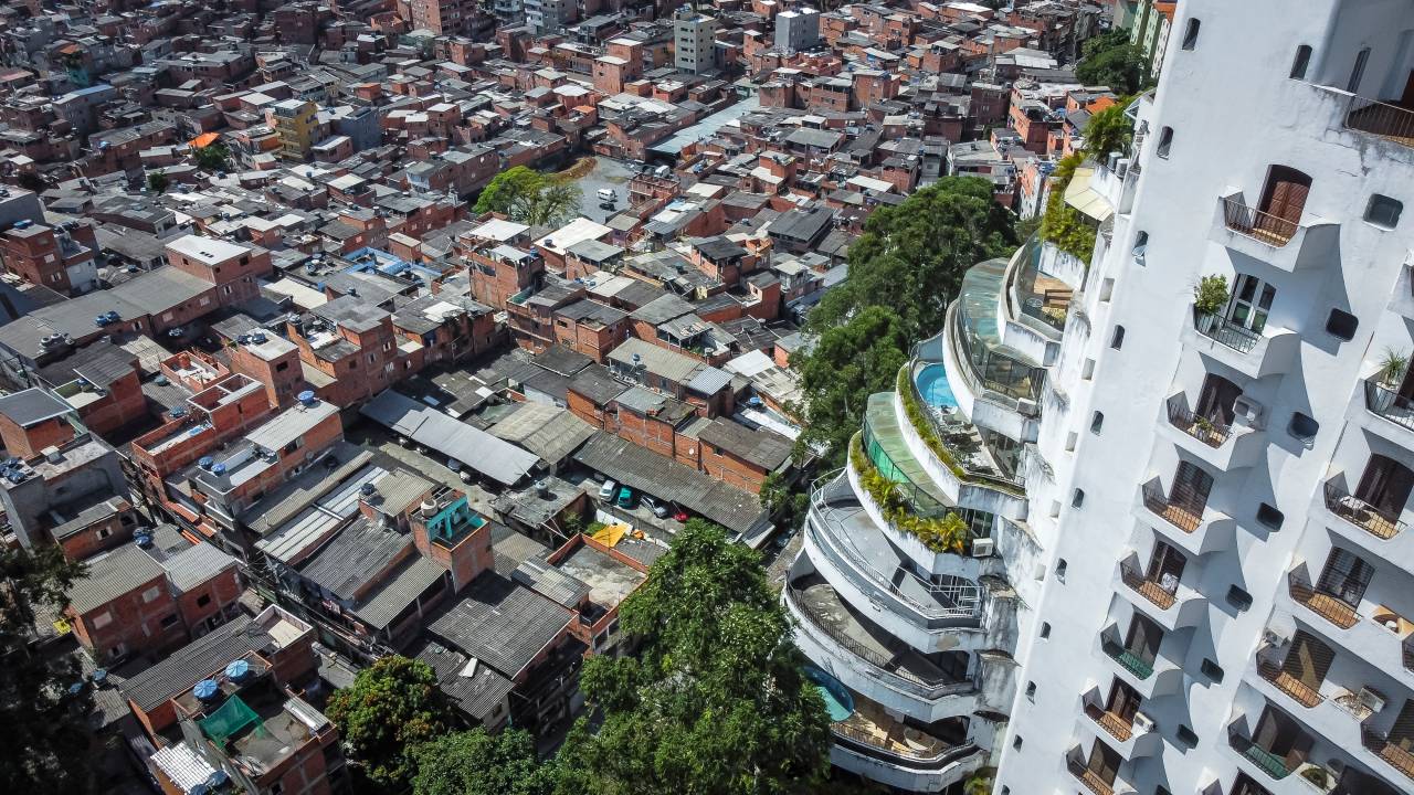 Imagem mostra foto aérea de prédio com uma piscina por andar, com sacadas em espiral e, ao lado, favela, com pequenas casas, a maior parte com tijolos expostos