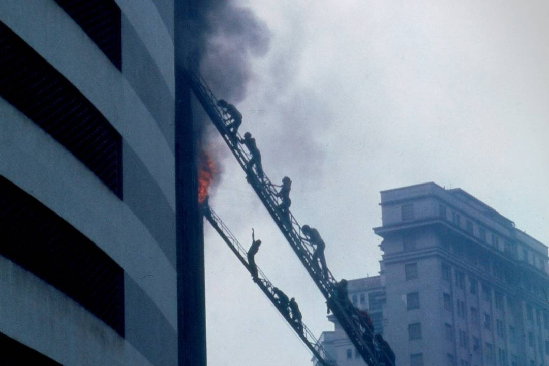 Foto histórica mostra escadas sendo erguidas até lateral de prédio em chamas, o Edifício Joelma
