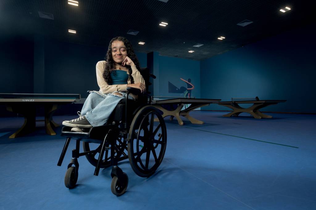Imagem mostra Nicole em centro de treinamento, em cadeira de rodas, sorrindo para foto, com o braço esquerdo apoiando a cabeça