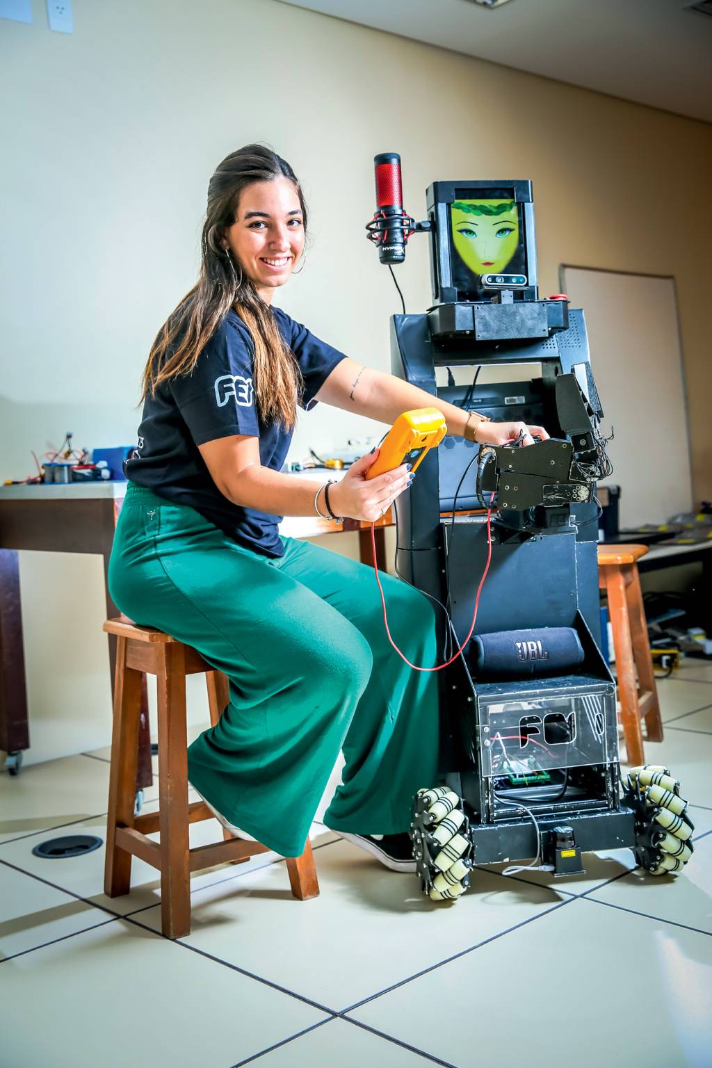 Imagem mostra jovem sentada ao lado de robô que tem tela com rosto. Ela segura aparelho e sorri para a foto