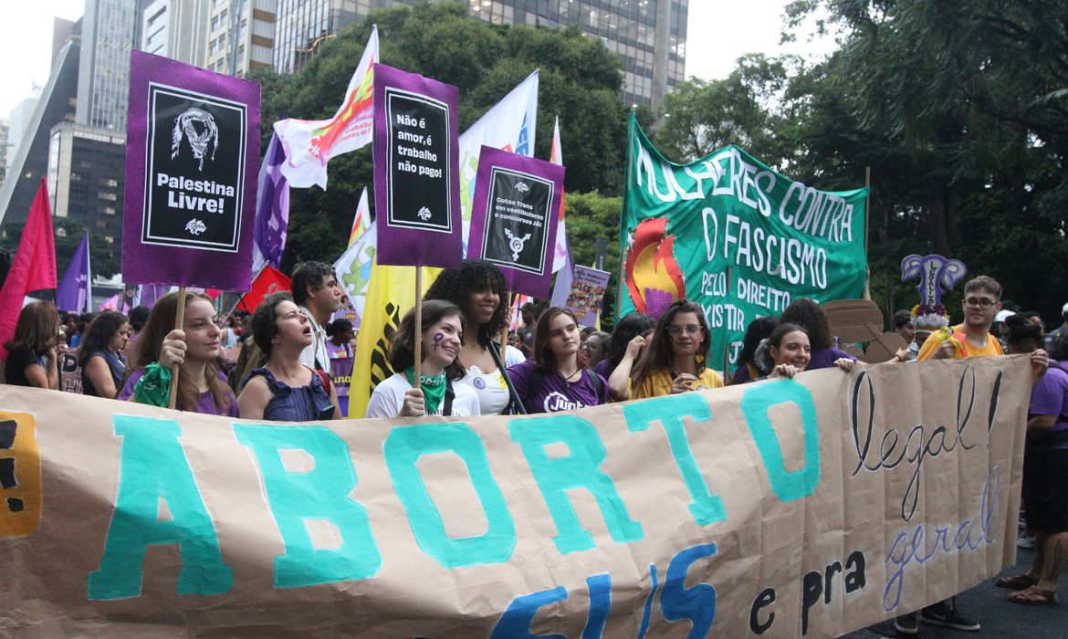 Foto de protesto com multidão de mulheres e faixas sobre aborto