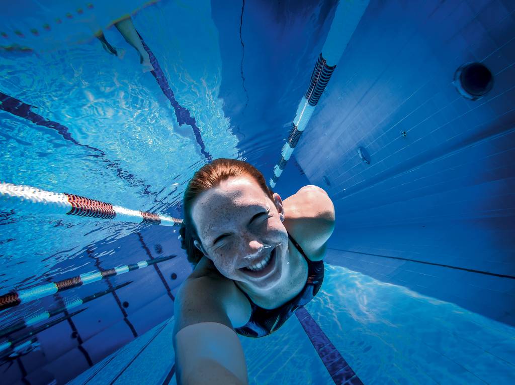 Imagem mostra Stephanie em piscina, sorrindo para foto embaixo da água