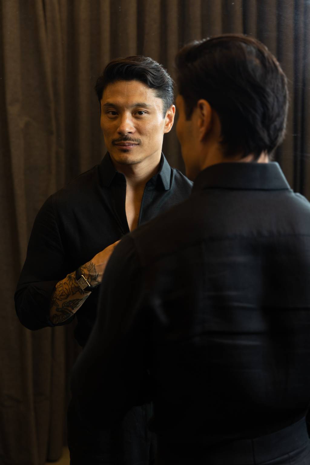 Homem asiático se encara no espelho vestindo camisa preta