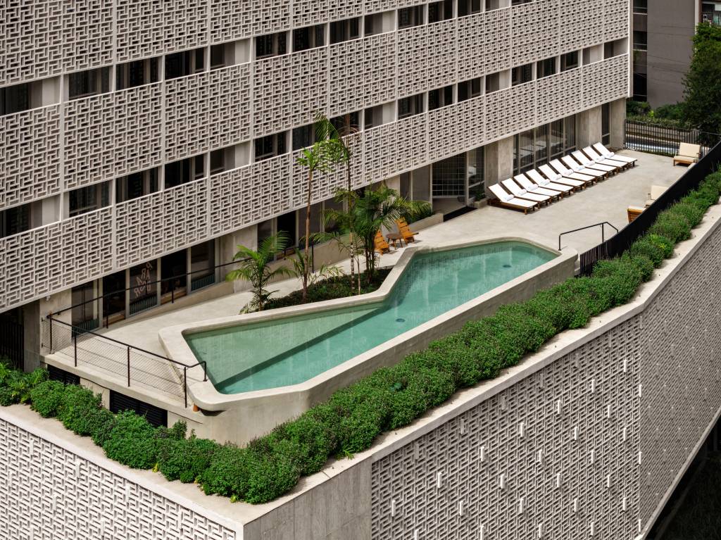 Vista aérea de prédio branco com parede vazada em pequenos quadrados e piscina no terraço da área inferior