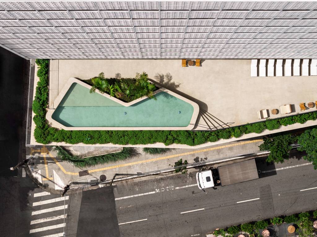 Vista aérea de prédio branco com parede vazada em pequenos quadrados e piscina no terraço da área inferior