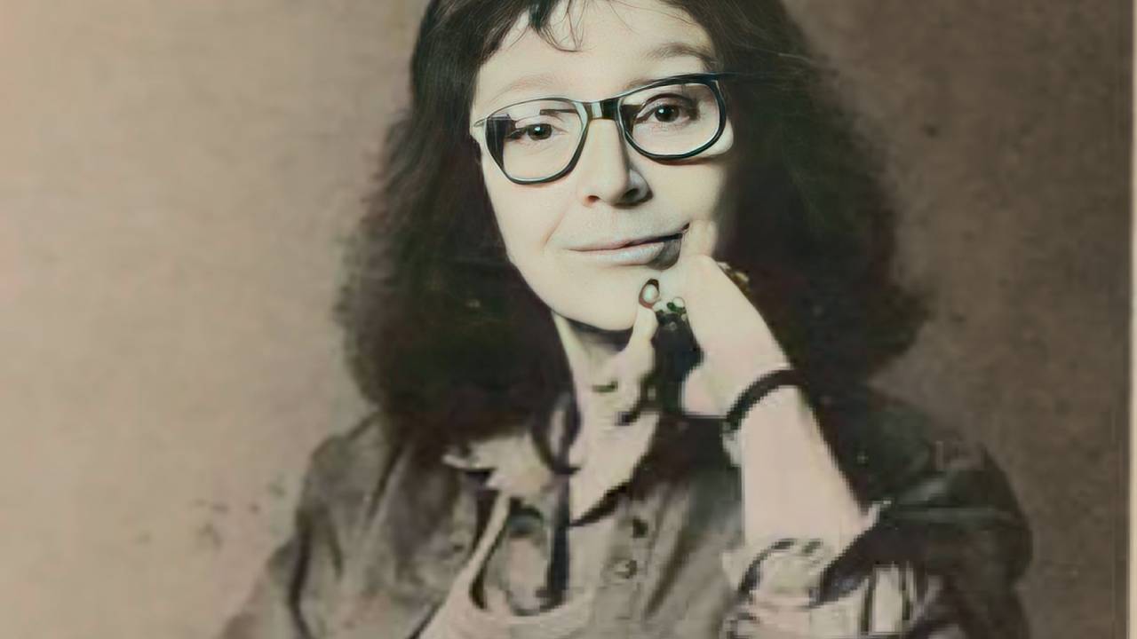 Retrato em preto e branco de mulher com mão no queixo, cabelos curtos e óculos