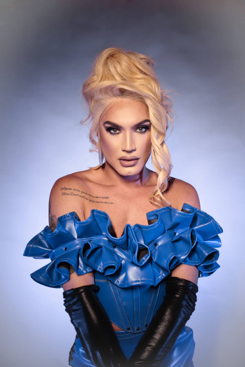 Aretuza Lovi-Crédito Maria Paula Freire-Divulgação (4) Drag queen loira veste traje azul com aparência de látex e babados na área do peito, além de luvas longas pretas.