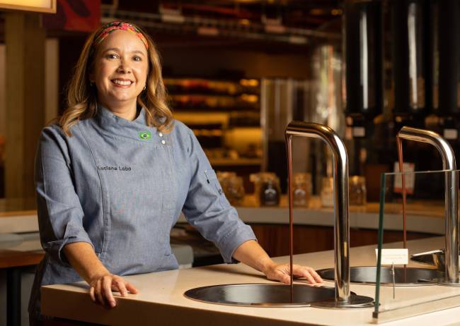 Mulher sorrindo em frente a uma bancada com uma torneira que sai chocolate.