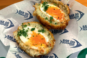 Bolovo de bacalhau cortado ao meio com a gema cremosa coberto por ervas frescas