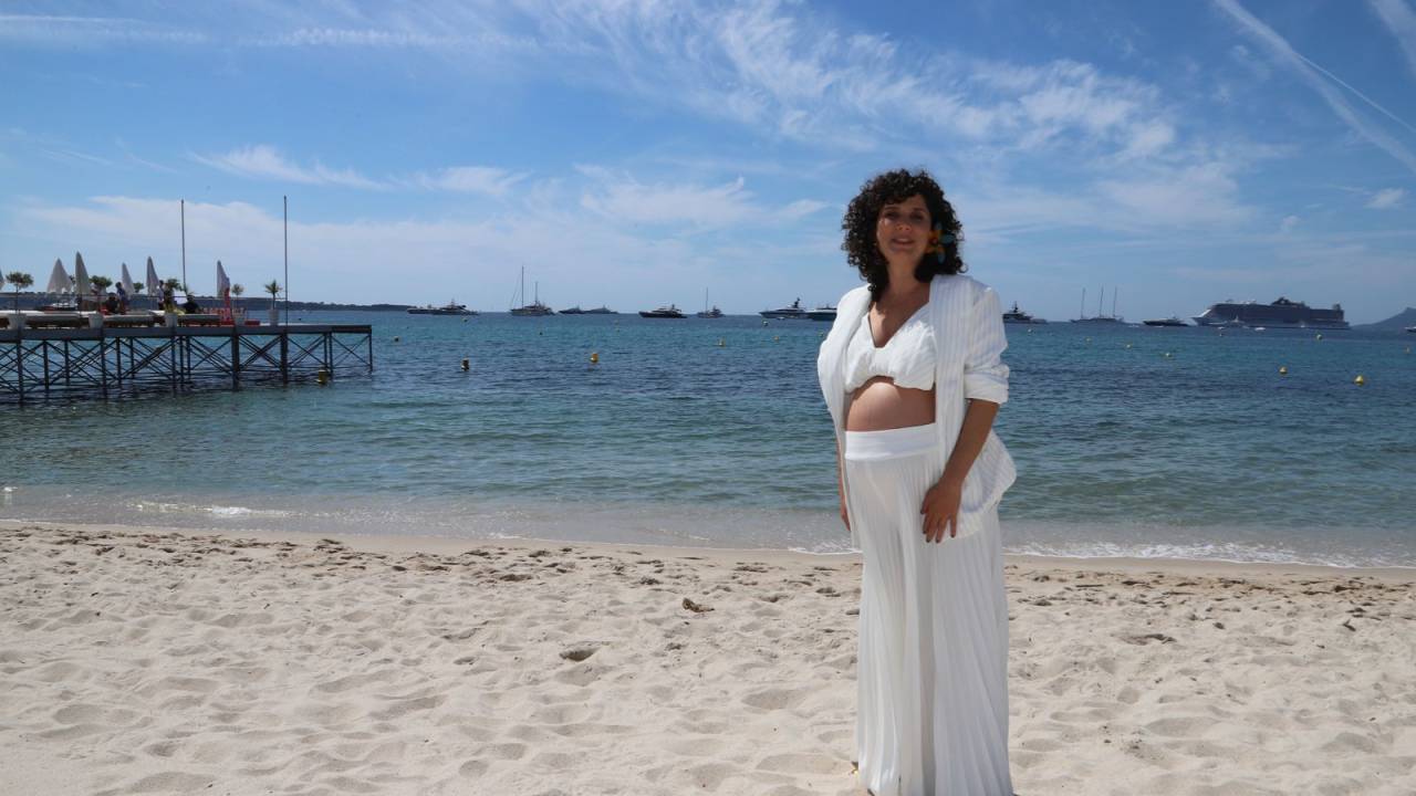 Mulher grávida com roupas brancas posa em praia