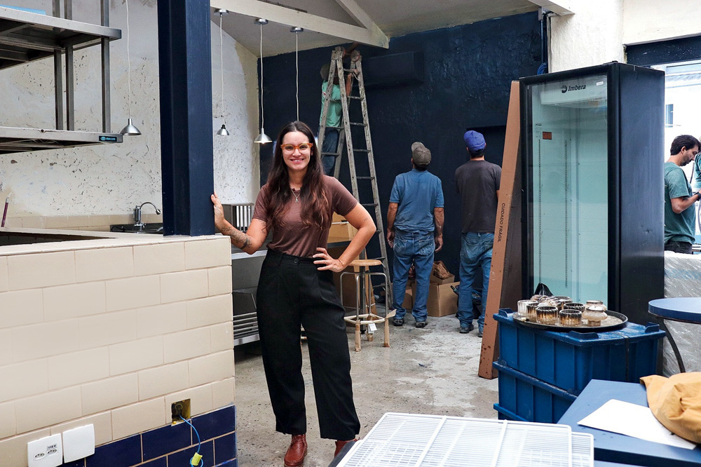 Mulher branca de cabelo preto sorrindo em meio a obra de restaurante.