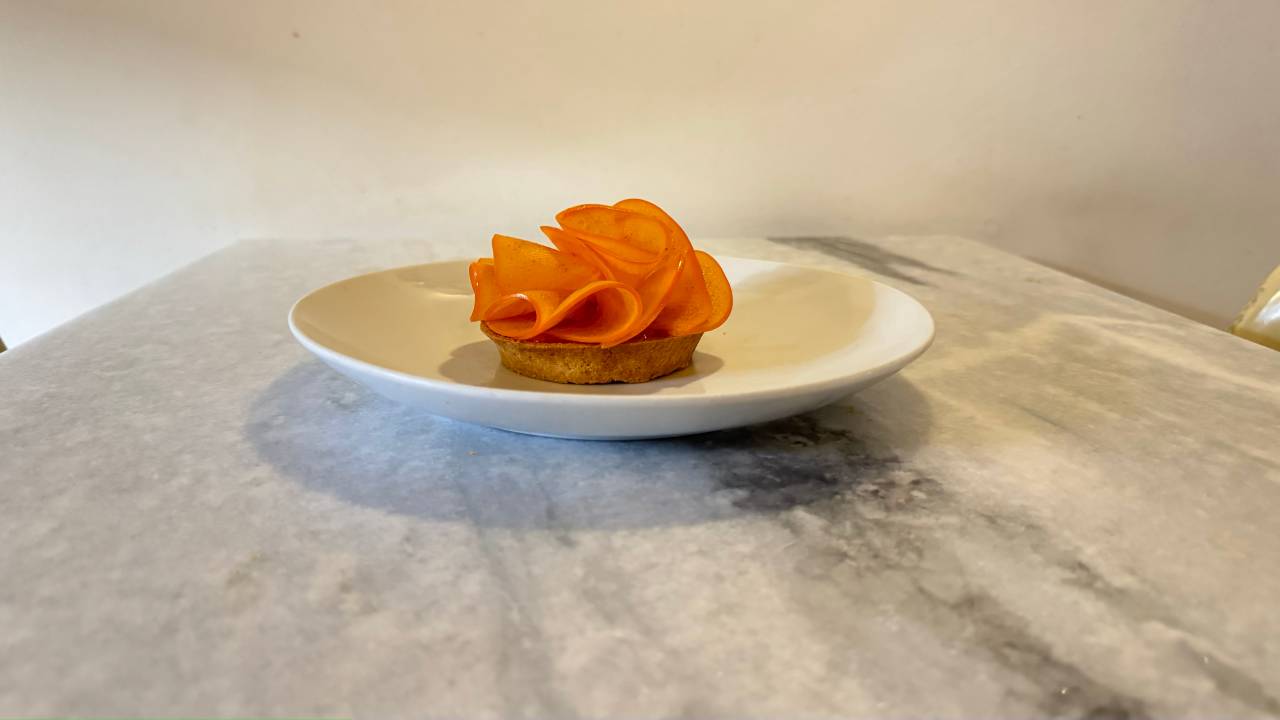 Prato de louça branca com tortinha coberta por "flor" feita com caqui.